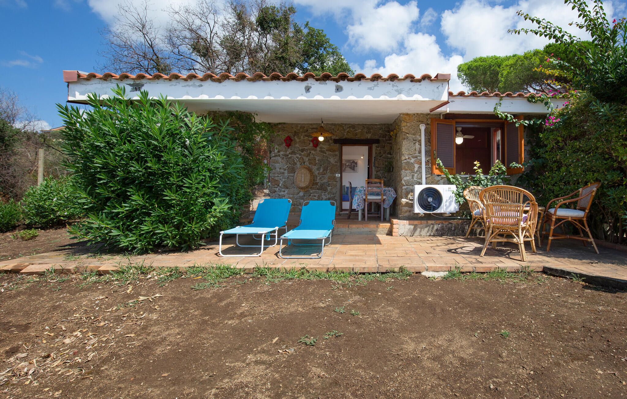 Een huis met een gevel van natuursteen, een overdekte patio met twee blauwe loungestoelen en een kleine tafel met rieten stoelen.