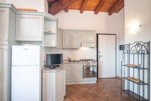 Une cuisine avec des meubles blancs, une cuisinière, un four, un réfrigérateur, un téléviseur et une étagère en métal.