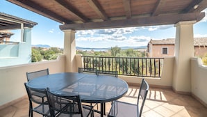 Eine überdachte Terrasse mit rundem Tisch und Stühlen, einer Holzbalkendecke und Blick auf die Landschaft.