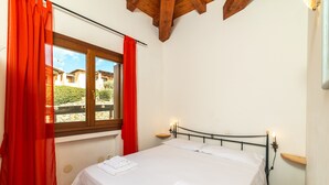 Ein Schlafzimmer mit einem Bett, roten Vorhängen, einem Fenster und einem Nachttisch mit einer Lampe.