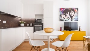 Une cuisine moderne avec des meubles blancs, un plan de travail en bois, une table ronde blanche avec deux chaises, un meuble jaune et un tableau accroché au mur.