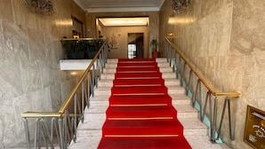 Un magnifique escalier recouvert d’un tapis rouge, avec des murs en marbre et de somptueux lustres.
