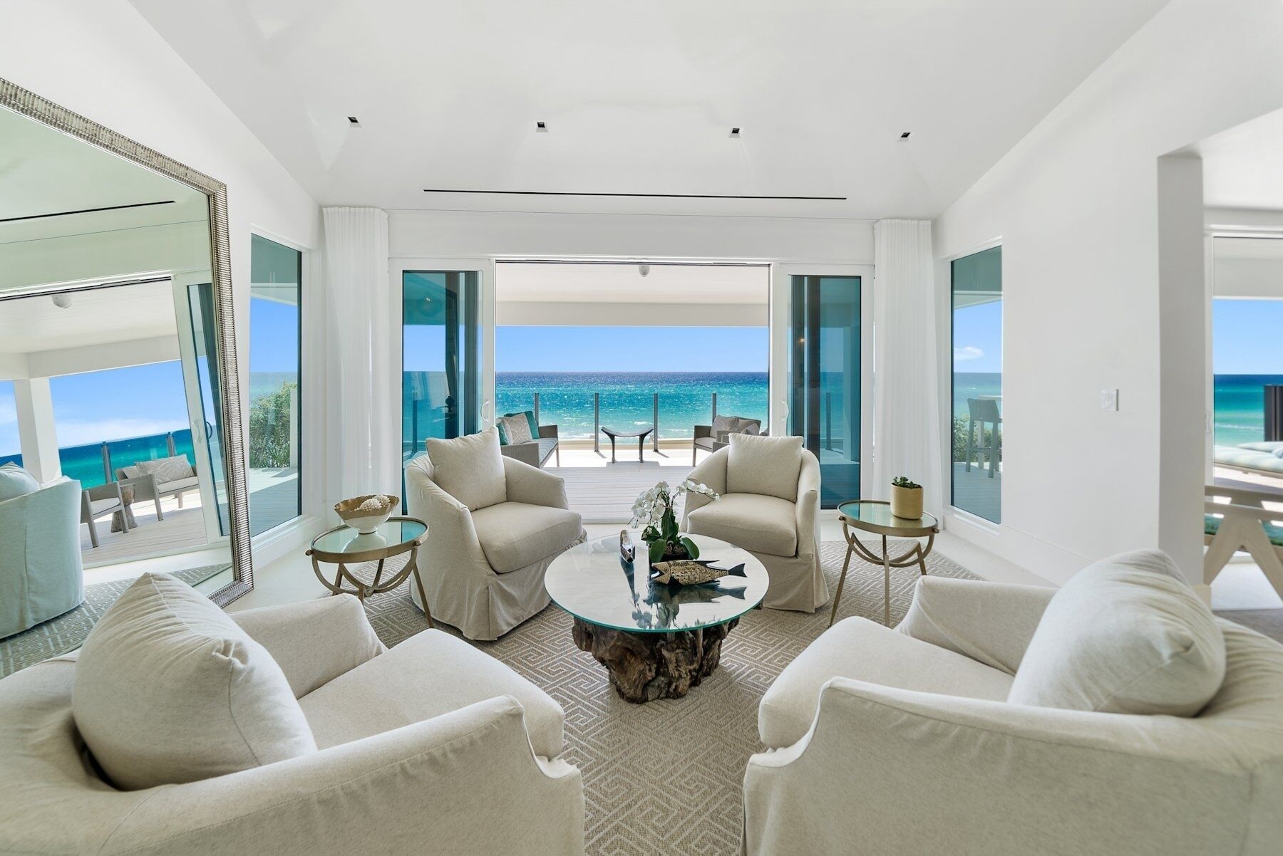 A modern living room with a large glass table, comfortable seating, and a view of the ocean.