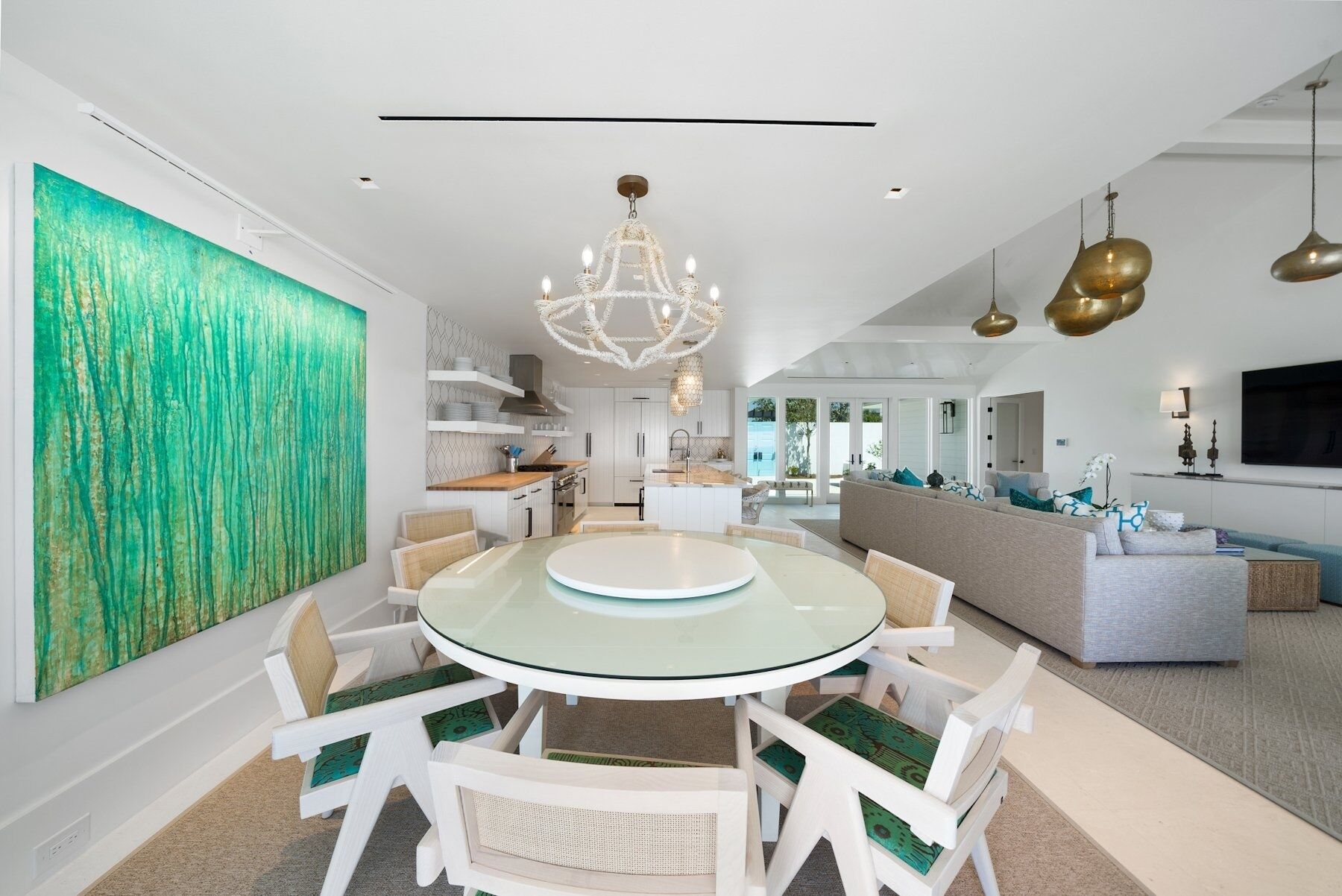 Une cuisine moderne avec des meubles blancs, une table de salle à manger ronde en verre et un grand tableau abstrait vert accroché au mur.