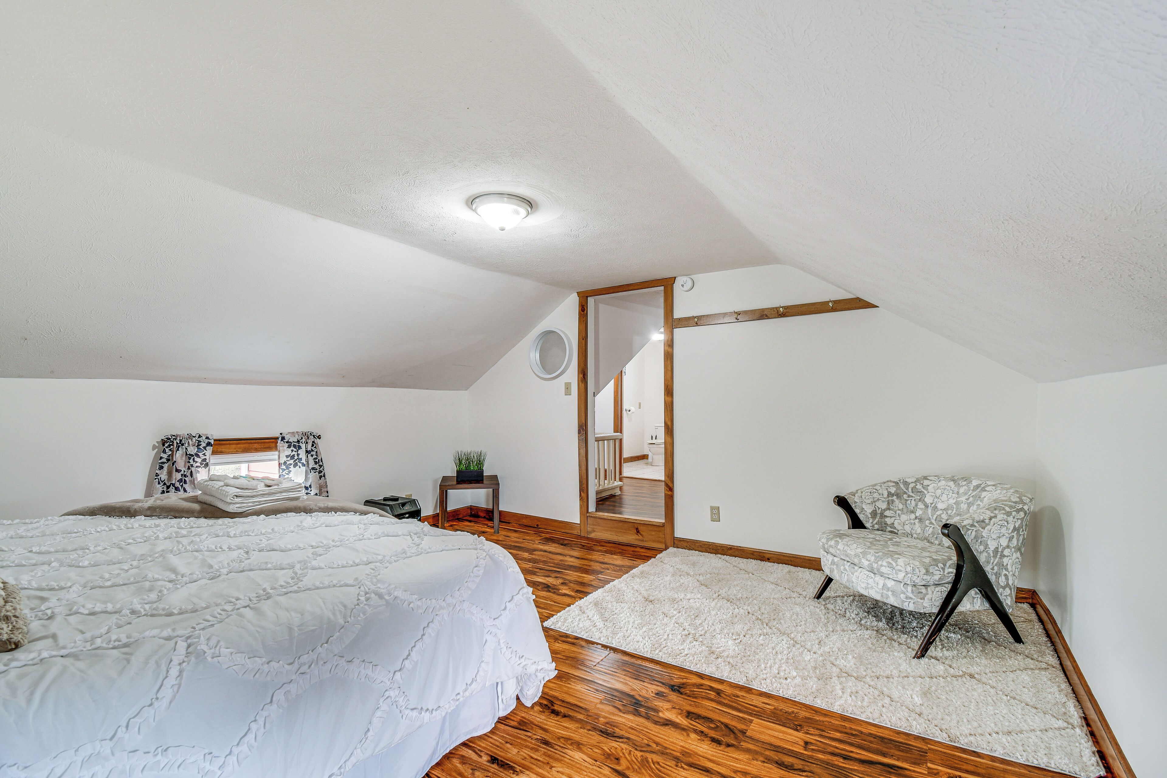 A bedroom with a large bed, a chair, a small table with a plant, and a mirror.