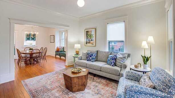 A spacious living room with a wooden dining table, a gray sofa, and a patterned rug.