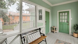 A porch with a bench, a green door, and a view of the neighborhood.