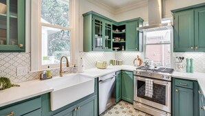 A kitchen with green cabinets, a white countertop, a stainless steel stove, and a window with a view of greenery.