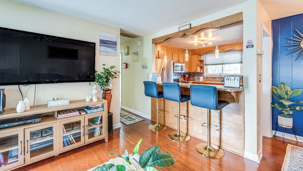 Een moderne woonkamer met een flatscreen televisie, een houten tv-meubel en een eethoek met barstoelen.