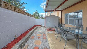 Eine Terrasse mit einem Glastisch und Stühlen, einer Ziegelwand und einem kleinen Schuppen.