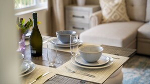 A dining table set with plates, bowls, glasses, and cutlery, with a bottle and a plant in the background.