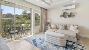 A spacious living room with a large sofa, a ceiling fan, and a balcony with outdoor furniture.