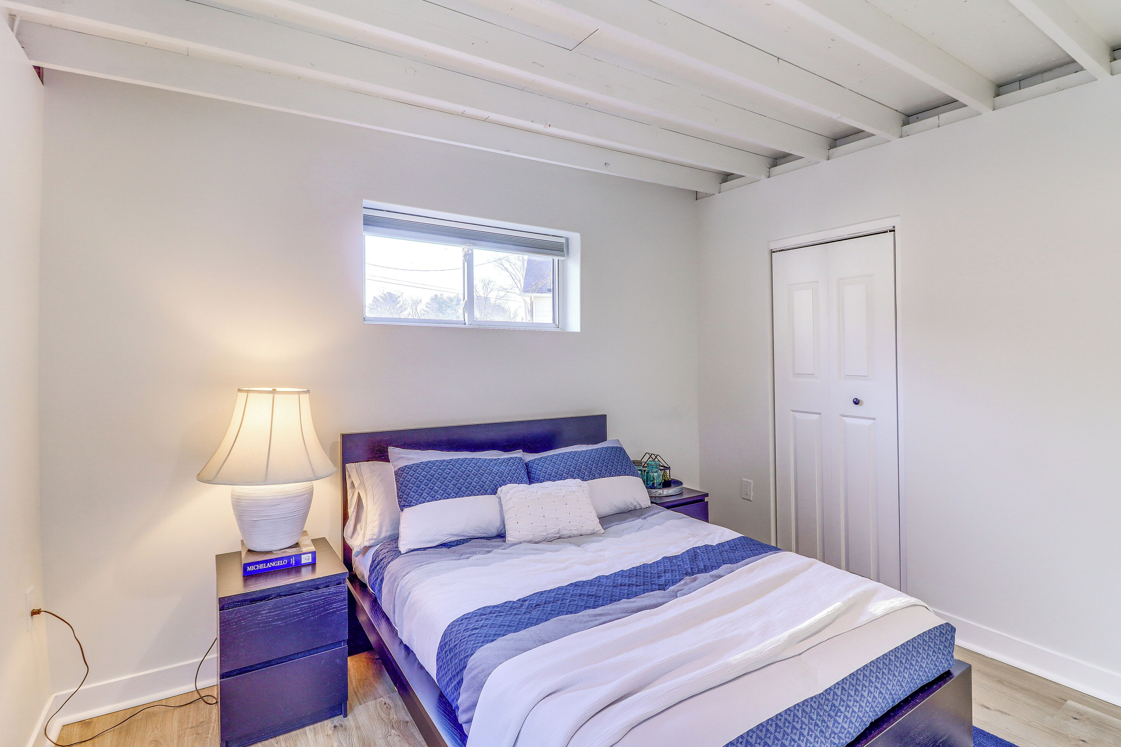 A bedroom with a bed, a nightstand with a lamp, a window, and a door.