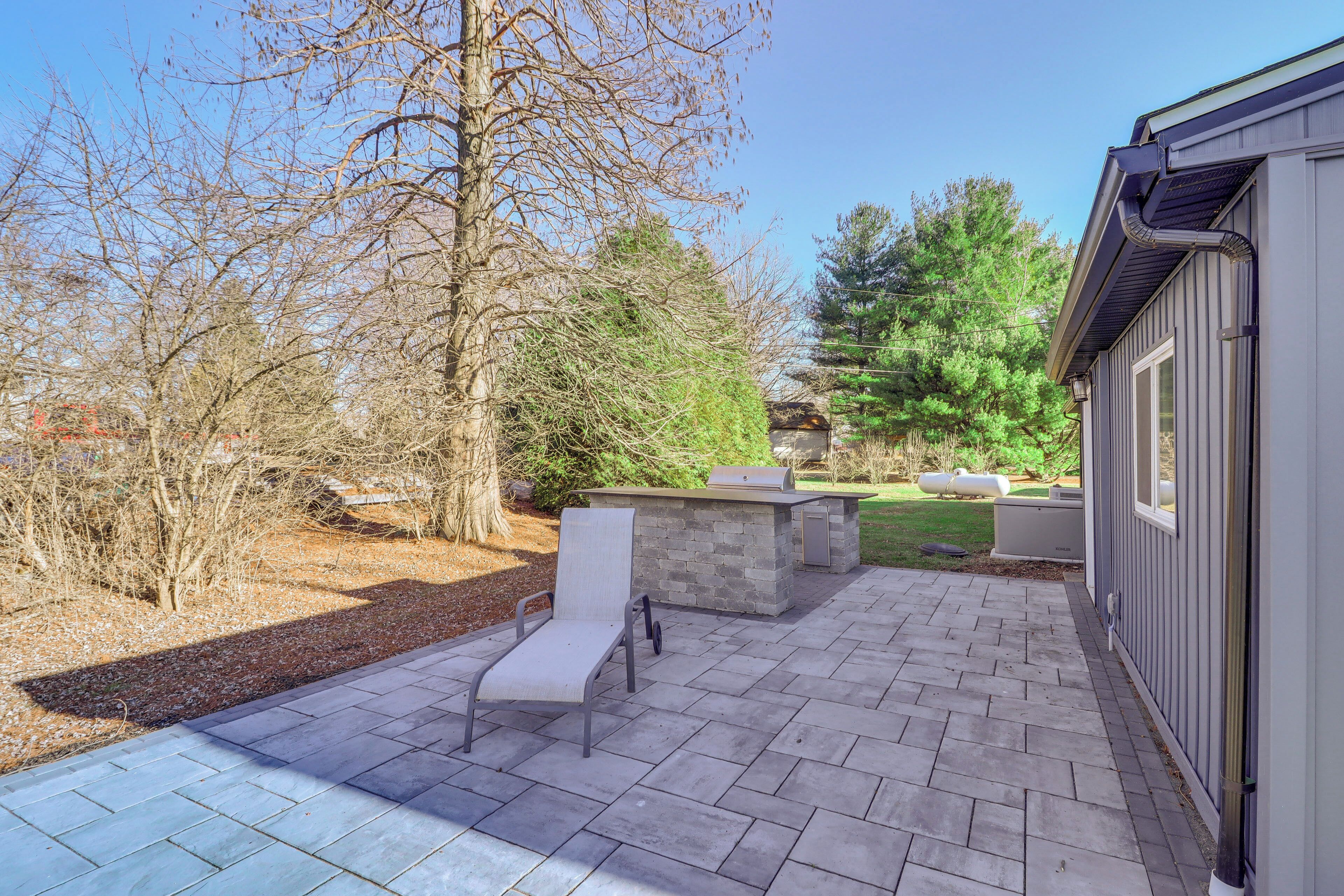 A patio with a stone fireplace, outdoor seating, and a view of a wooded area.
