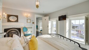 A bedroom with a bed, a mirror, a chandelier, and a door leading to another room. - Oceanfront Mid-coast Maine Home w/ Private Beach! (Stockton Springs)