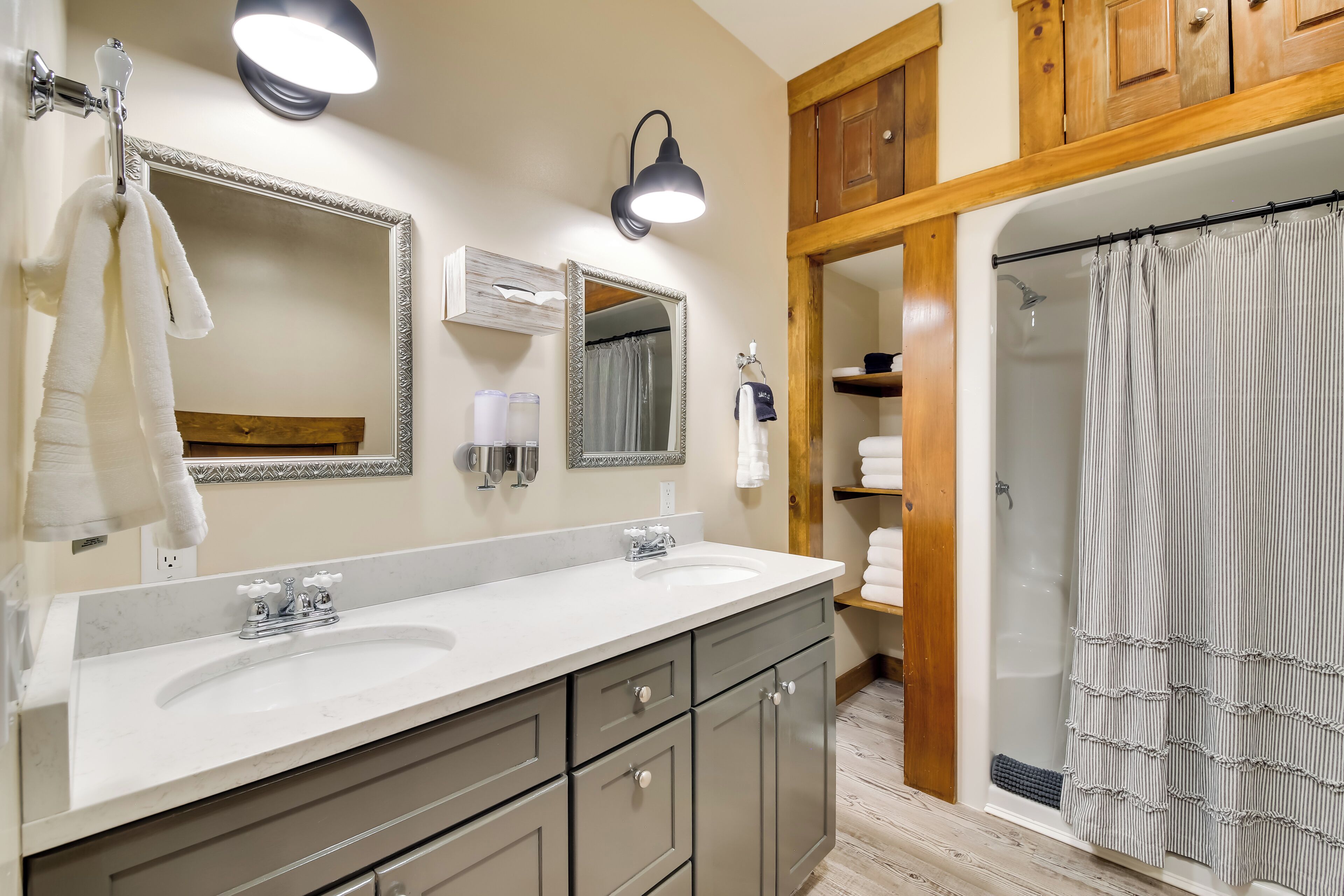 A bathroom with two sinks, a mirror, a shower, and wooden cabinets.