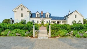A large, white, two-story house with a brick chimney, a covered front porch, and a gravel driveway leading to a stone entrance. - Oceanfront Mid-coast Maine Home w/ Private Beach! (Stockton Springs)