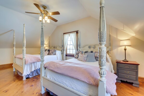 A bedroom with two four-poster beds, a ceiling fan, a nightstand, and a window with curtains.