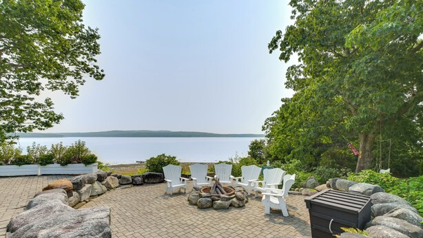 A patio with white chairs, a fire pit, and a view of a lake. - Oceanfront Mid-coast Maine Home w/ Private Beach! (Stockton Springs)