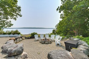 A patio with white chairs, a fire pit, and a view of a lake.