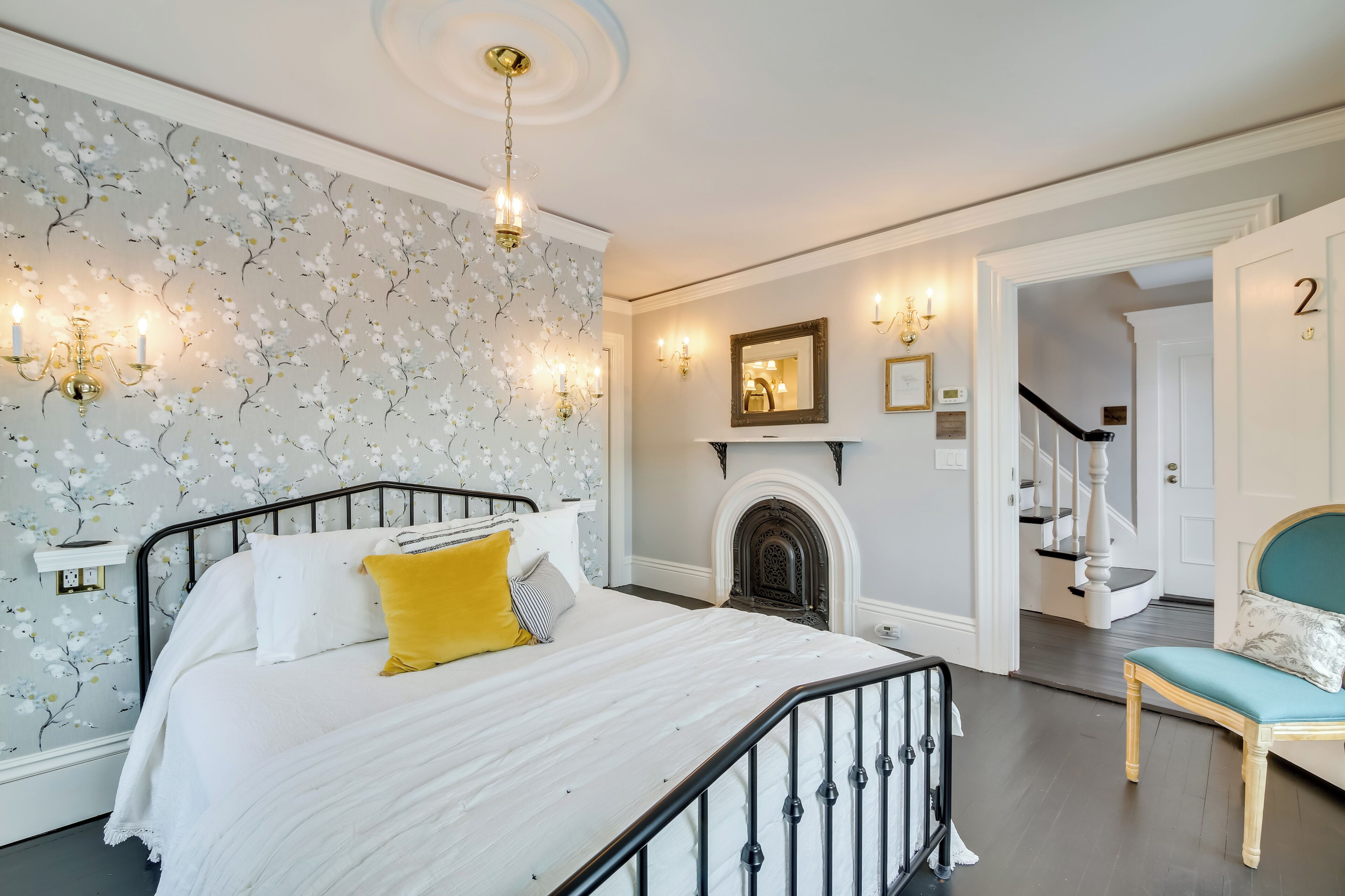 A bedroom with a bed, a chair, a fireplace, and a staircase.