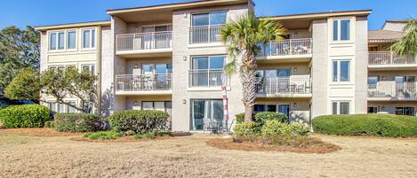 A multi-story apartment building with balconies, a palm tree, and a well-maintained lawn.
