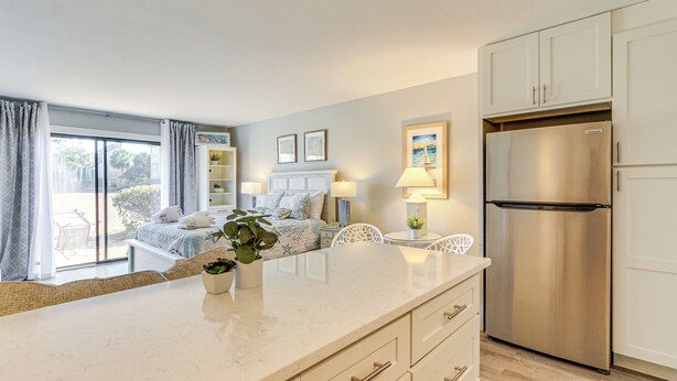 Eine moderne Küche mit einem Edelstahlkühlschrank, ein Essbereich mit Tisch und Stühlen sowie ein Schlafzimmer mit Bett und Fenster.