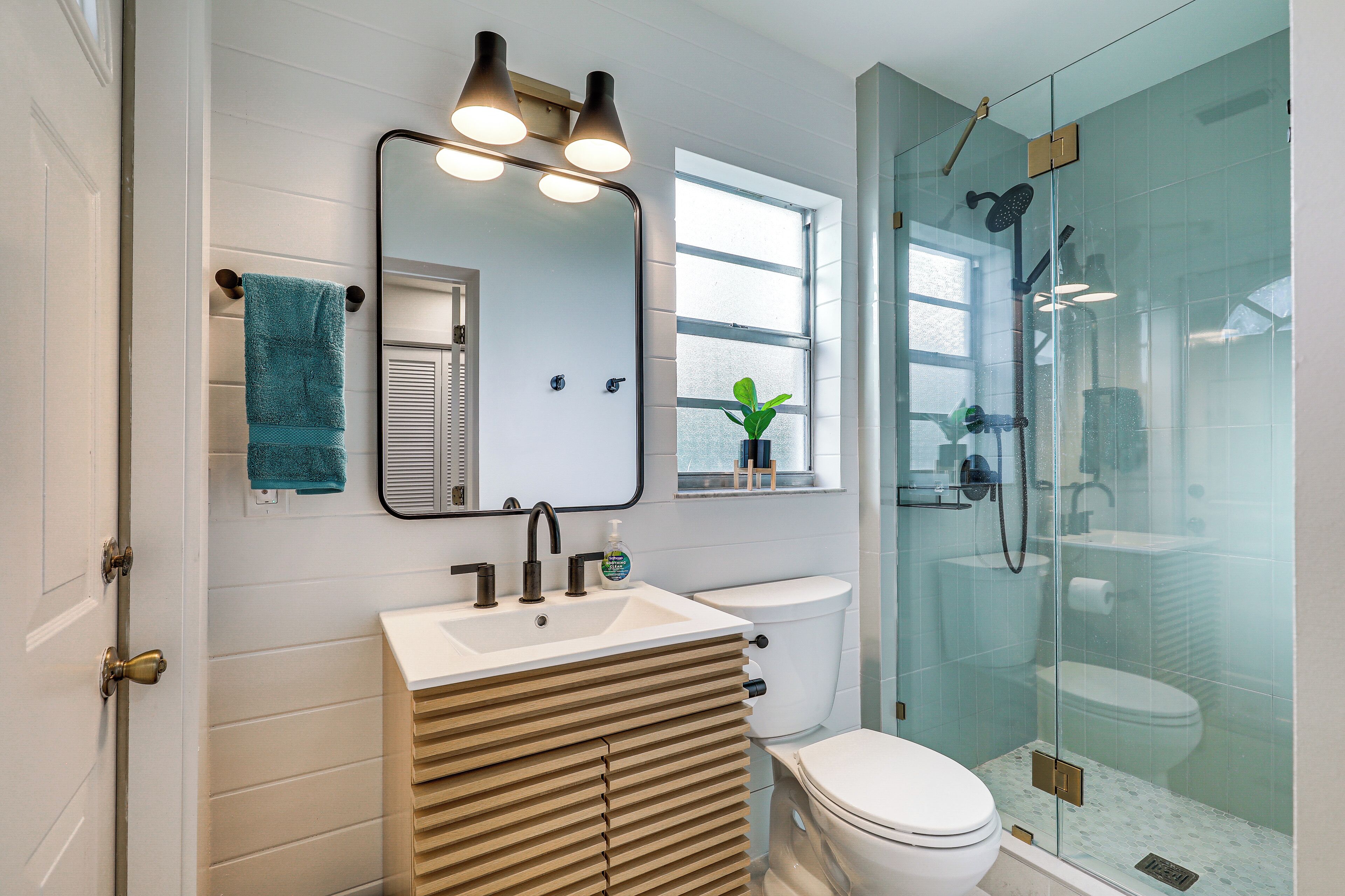 A modern bathroom with a large mirror, a sink, a toilet, and a glass-enclosed shower.