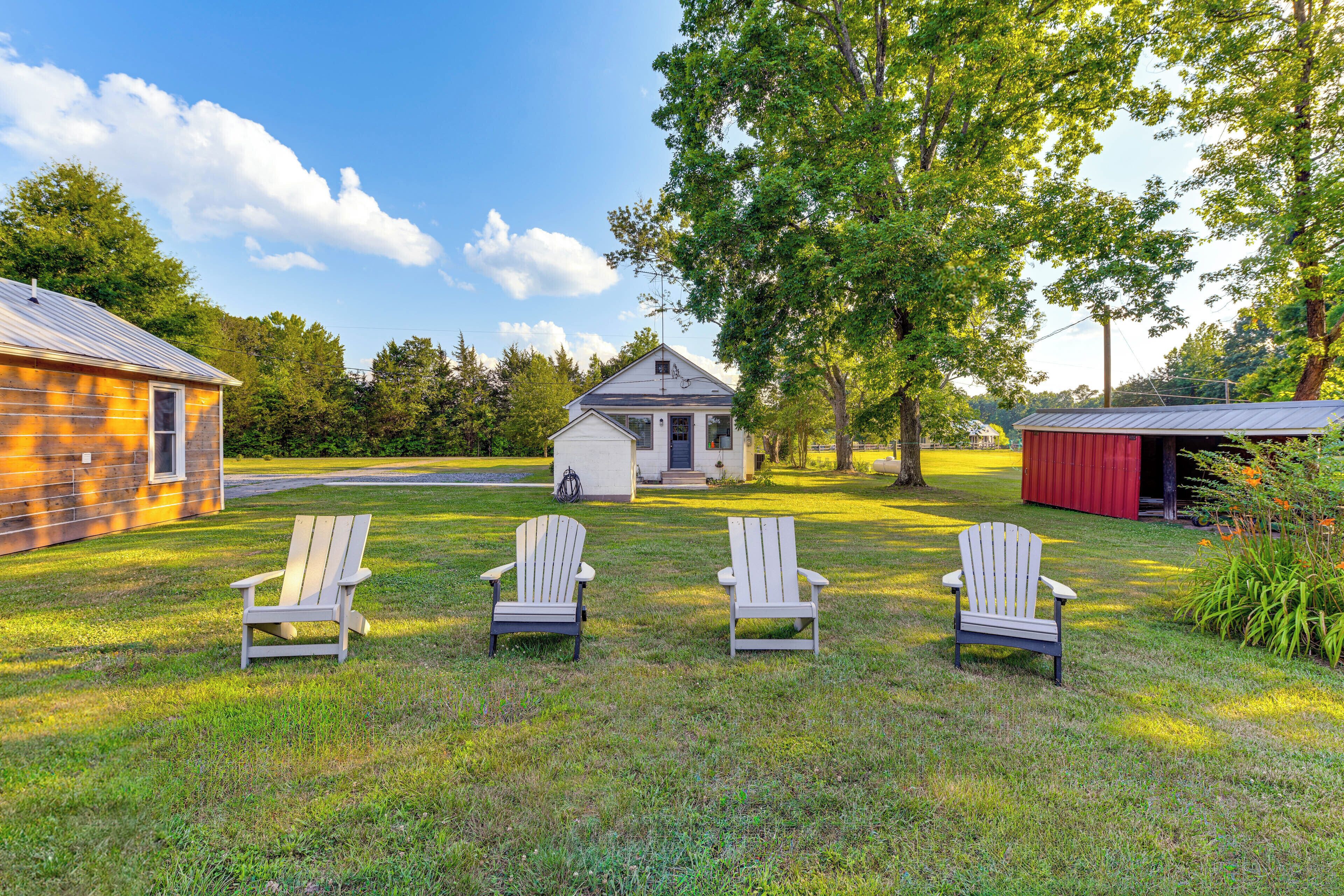Une zone herbeuse avec trois fauteuils Adirondack, un petit bâtiment blanc et une grange rouge.