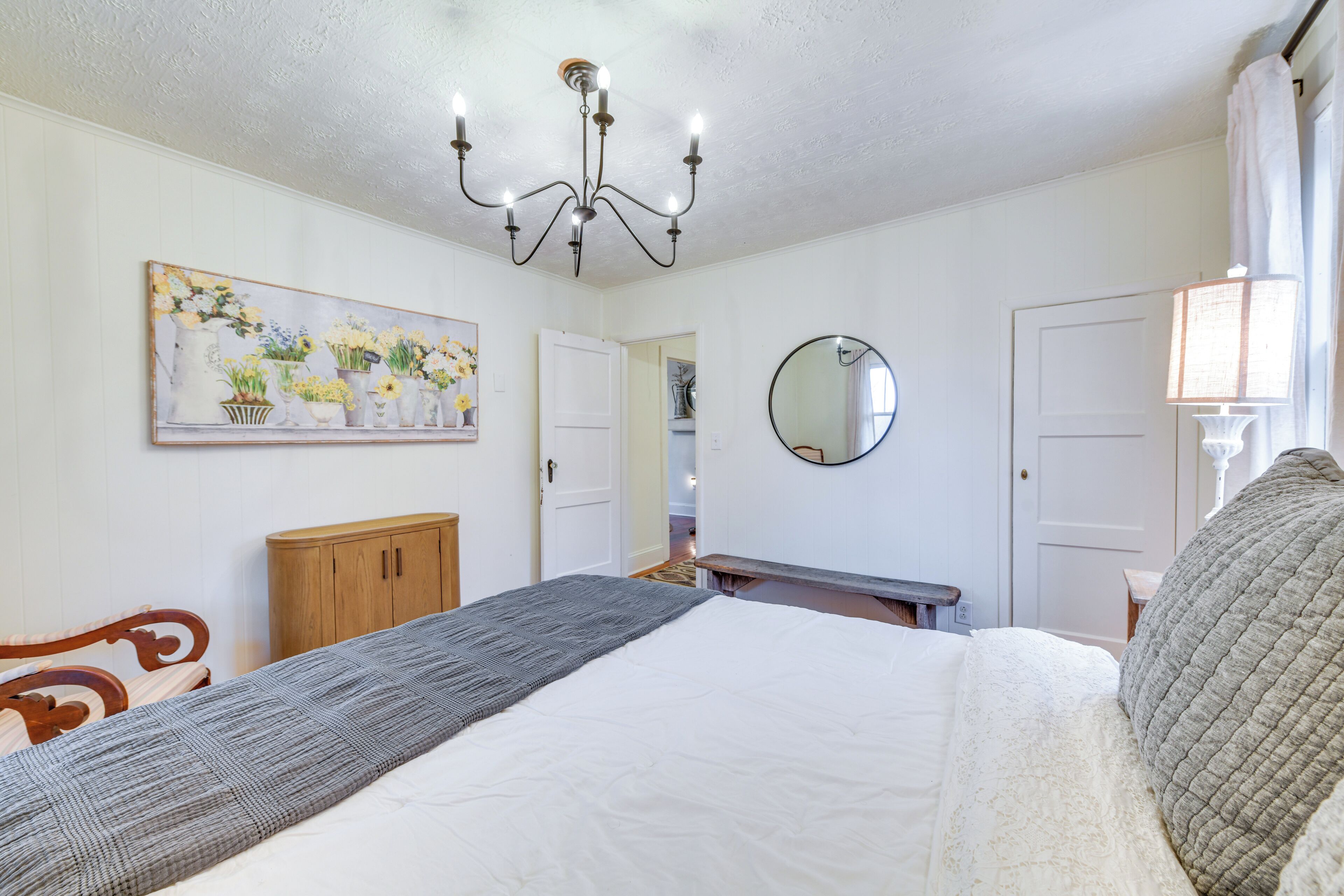 A bedroom with a bed, a wooden cabinet, a painting, a mirror, and a chandelier.