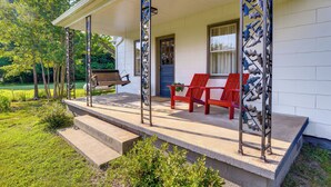 A covered porch with a bench and red chairs, a door, and a metal sculpture.
