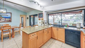 A kitchen with wooden cabinets, granite countertops, a dishwasher, and a large window with a view of the outside. - Marco Island Home w/ Private Pool & Water Views! (Marco Island)