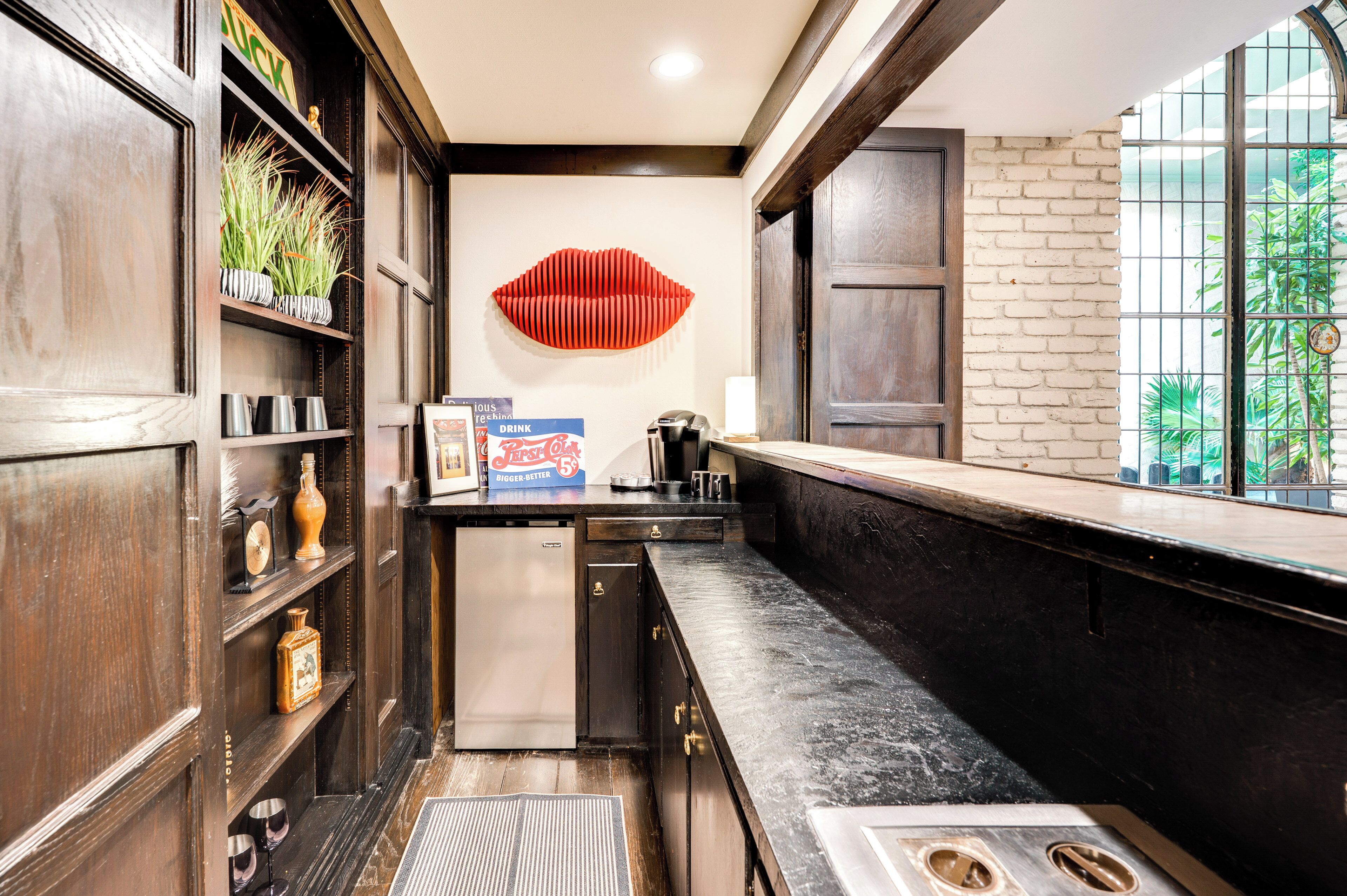 A kitchen with wooden cabinets, a refrigerator, a countertop, and a window with a view of greenery.