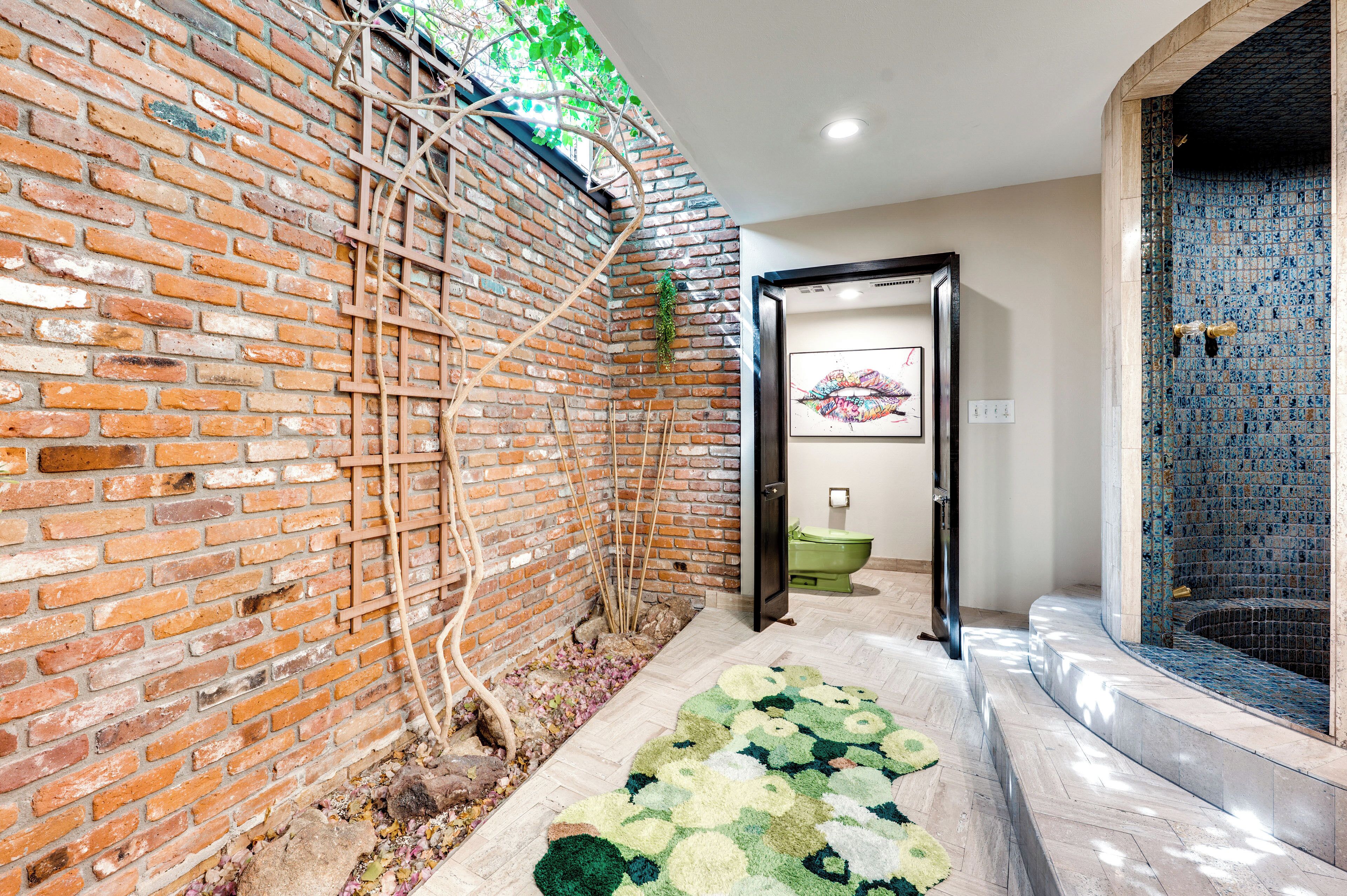 A bathroom with a brick wall, a green toilet, and a mosaic-tiled bathtub.