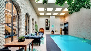 An indoor swimming pool area with a brick wall, a wooden table, and a sofa. - Heated Pool: Tropical Townhome in Wheat Ridge (Wheat Ridge)