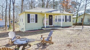 A small, single-story house with a porch, a small deck, and a yard with a fire pit and Adirondack chairs. - Pet-friendly Georgia Retreat w/ Fire Pit & Porch! (Forest Park)
