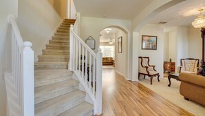 A staircase with a white railing leading to a second floor. A wooden floor extends through the space, and there are two upholstered chairs and a small table. - Spacious Vacation Rental w/ Yard in Kissimmee! (Kissimmee)