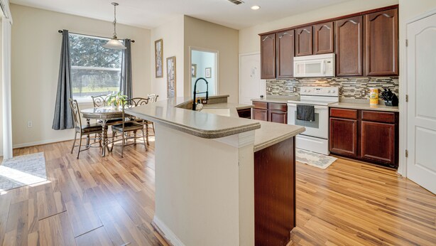 A spacious kitchen with wooden cabinets, a central island, and a dining area with chairs and a table. - Spacious Vacation Rental w/ Yard in Kissimmee! (Kissimmee)