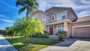 A two-story house with a red door, a garage, and a well-maintained lawn with palm trees. - Spacious Vacation Rental w/ Yard in Kissimmee! (Kissimmee)