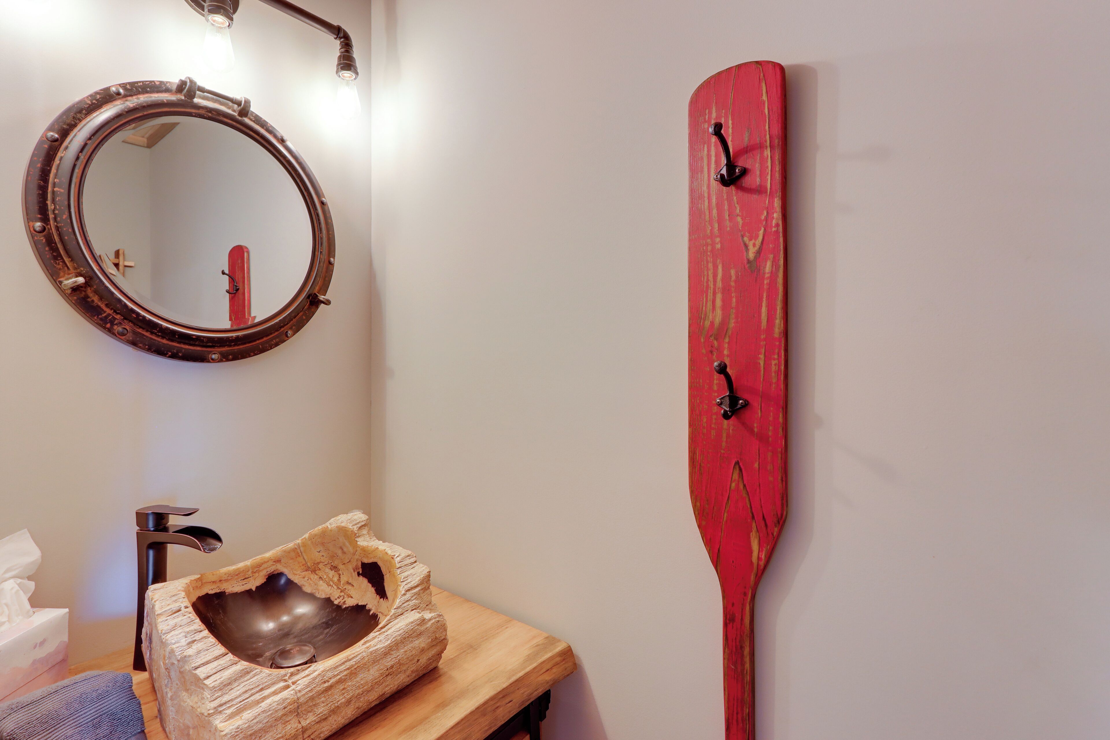 Un bagno con un lavabo in legno, uno specchio rotondo e una decorazione murale a forma di pagaia rossa.