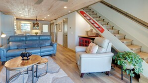 A spacious living room with a blue sofa, a white armchair, and a wooden coffee table. A staircase with a red railing leads to an upper level. - Lakefront Townhome w/ Dock: 6 Mi to Blue Ridge! (Morganton)