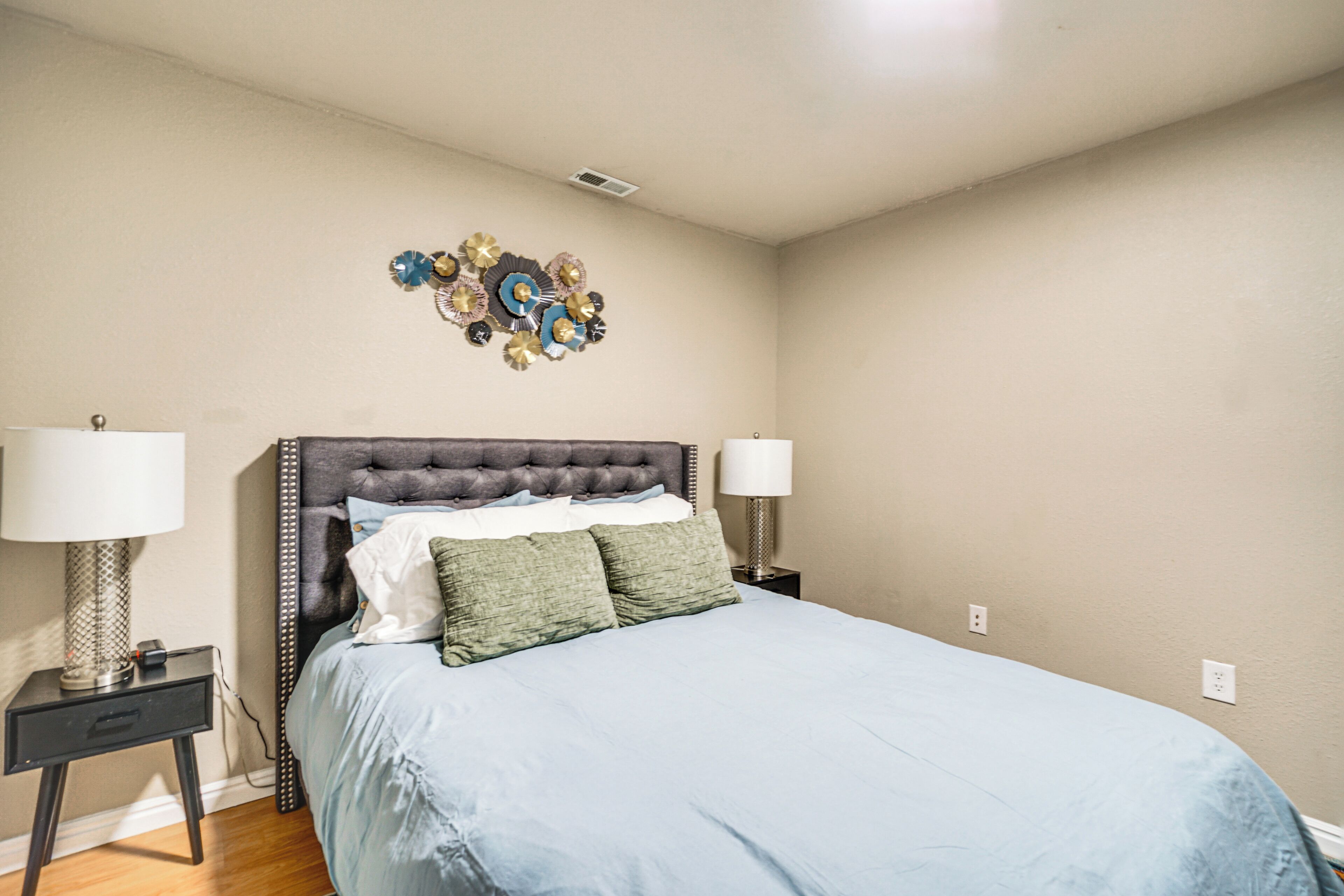 A bedroom with a large bed, two bedside tables, and a decorative wall piece.
