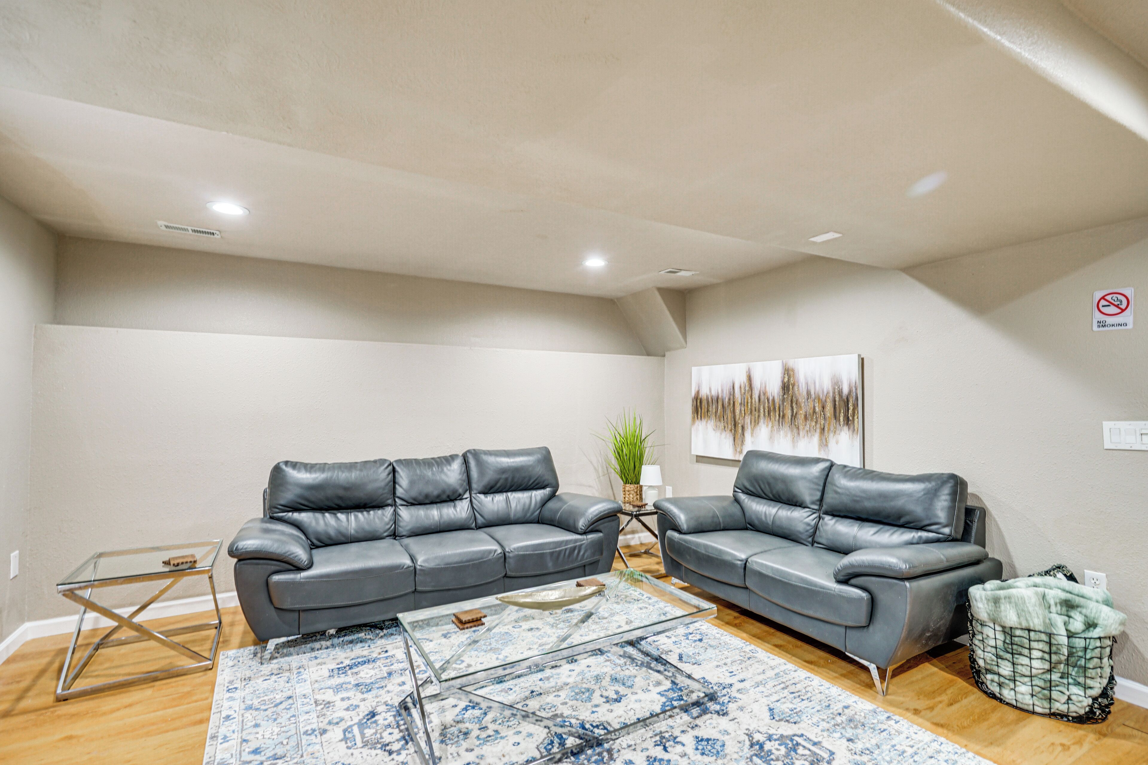 A living room with two grey leather sofas, a glass coffee table, and a patterned rug.