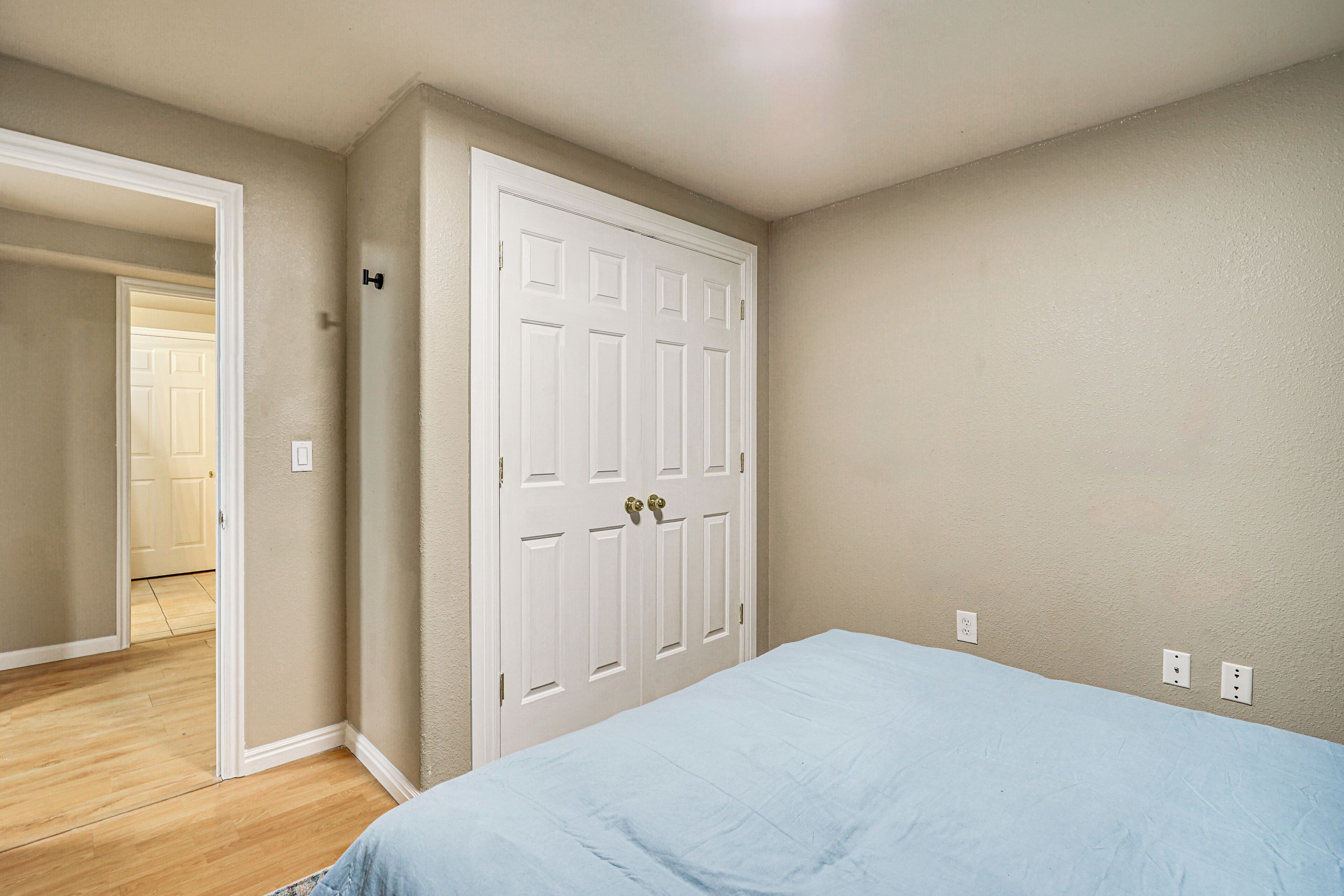 Un dormitorio con una cama, una puerta blanca e interruptor de luz en la pared.