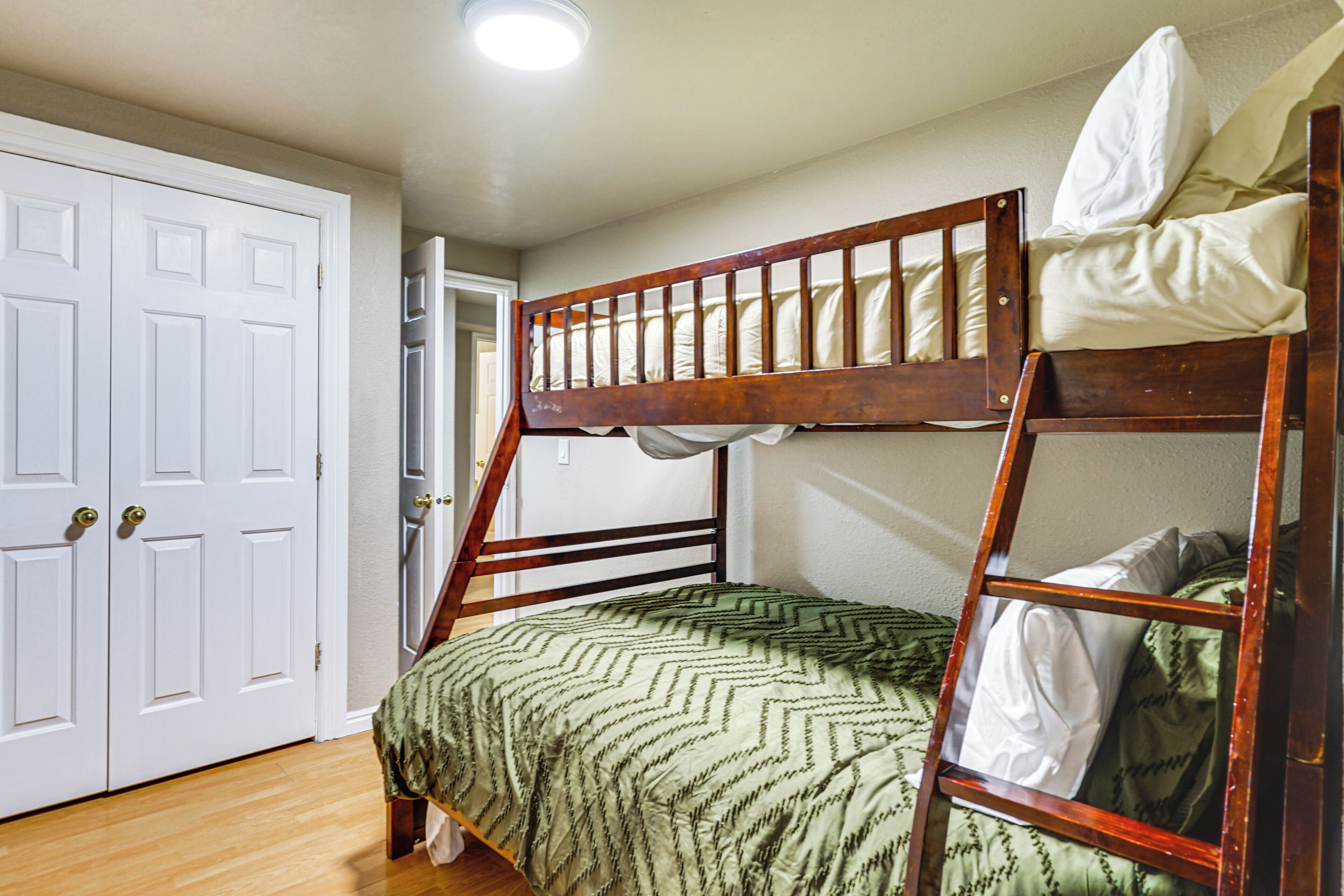 A bunk bed with a green patterned bedspread, a wooden ladder, and white pillows.