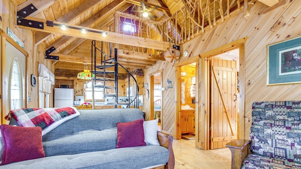 A cozy cabin interior with a wooden ceiling, a sofa with a blanket, and a patterned chair. - Quaint Dahlonega Cabin w/ Cavenders Creek Access! (Dahlonega)