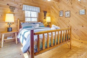 Quarto de cabana de madeira com uma cama, duas mesas de cabeceira, uma janela e luminárias fixadas na parede.