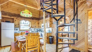 A wooden cabin interior with a dining area, kitchen, and a spiral staircase. - Quaint Dahlonega Cabin w/ Cavenders Creek Access! (Dahlonega)