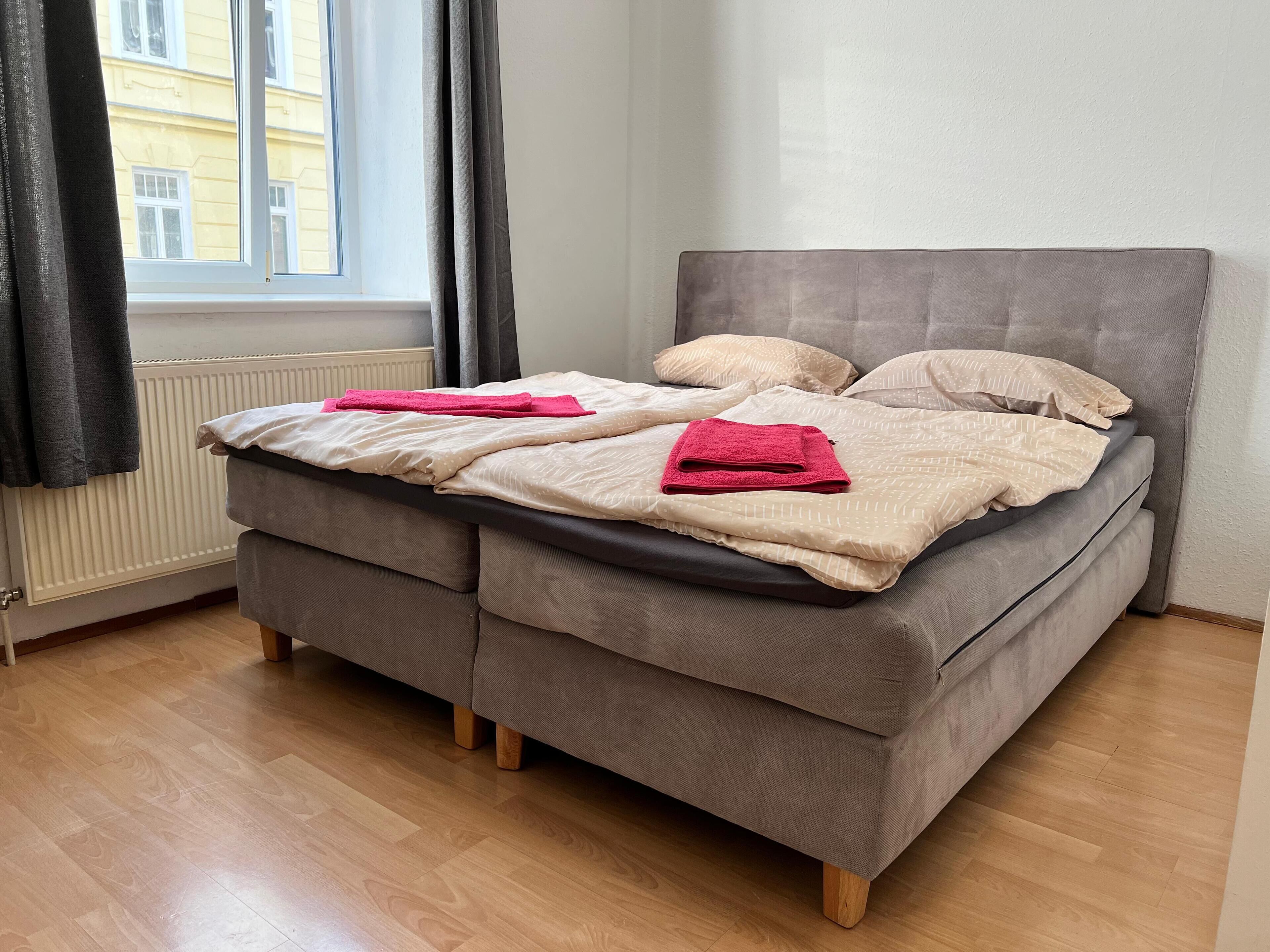 A double bed with a grey headboard and two pillows, a window with curtains, and a radiator.