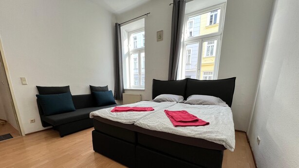 Une chambre moderne avec un grand lit, un canapé et une vue sur les immeubles par la fenêtre.